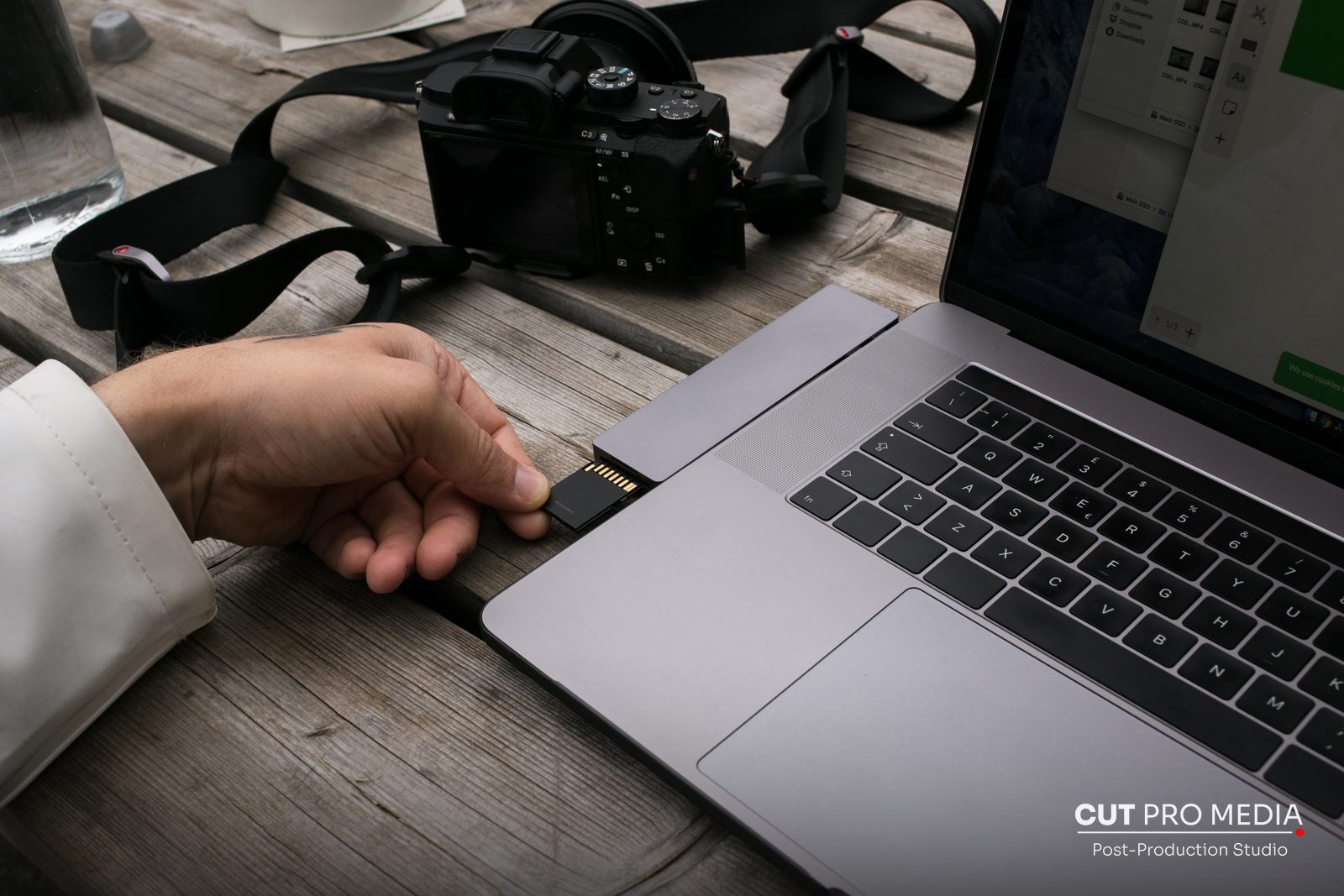Hand inserting a memory card into a laptop next to a camera